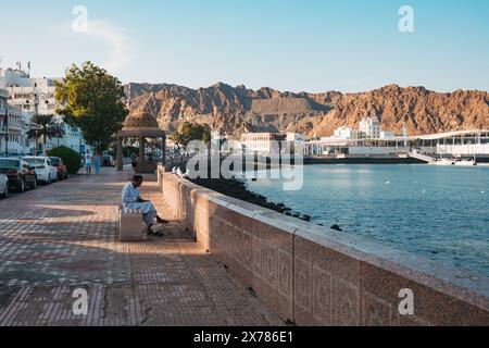 Ein Mann sitzt auf einer Bank auf der Corniche im Sultan Qaboos Port, Maskat, Oman, bei Sonnenuntergang Stockfoto