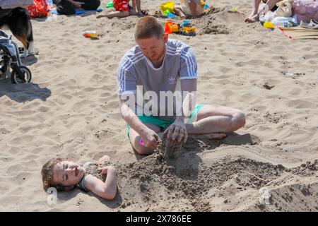 Troon, Großbritannien. Mai 2024. Touristen und Einheimische genießen das warme und sonnige Wetter am Troon Beach, South Ayrshire, Schottland, trotz eines rollenden Nebels am Nachmittag, der vom Firth of Clyde kommt. Bild von Callum Kerr aus Glasgow, der seine Tochter Olivia im Alter von vier Jahren im Sand bedeckt. Quelle: Findlay/Alamy Live News Stockfoto