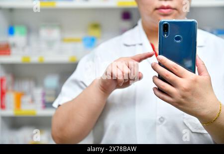 Ein Apotheker hält ein Mobiltelefon, um ein ärztliches Rezept zu erhalten, Medikamente zuzubereiten und Medikamente in einer Apotheke zu überprüfen. Stockfoto