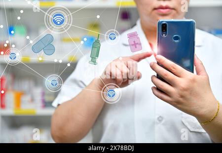 Ein Apotheker hält ein Mobiltelefon, um ein ärztliches Rezept zu erhalten, Medikamente zuzubereiten und Medikamente in einer Apotheke zu überprüfen. Stockfoto