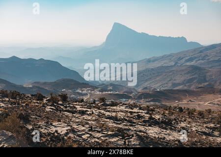 Riesige Berglandschaft in Jebel Shams, Oman, mit mehrschichtigen Graten und einem hohen Gipfel in der Ferne unter einem trüben Himmel. Stockfoto