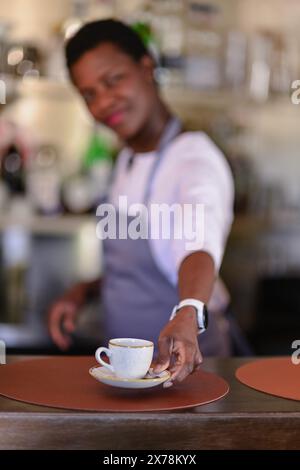 Ein freundlicher Barista auf einer Schürze serviert eine Tasse Kaffee in einer warmen und einladenden Café-Atmosphäre Stockfoto