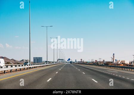 Moderne, leere Autobahn in Oman mit Schildern für Geschwindigkeitsbegrenzungen, Straßenlaternen und klarem blauen Himmel, die Straßeninfrastruktur und Verkehrsmittel zeigen Stockfoto