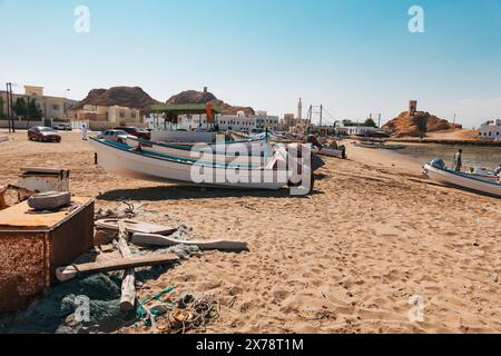 Fischerboote fuhren an einem Sandstrand in Sur, Oman, mit Netzen, Ausrüstung und traditionellen Küstengebäuden im Hintergrund Stockfoto