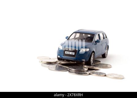 Blaues Spielzeugauto mit Münzen auf weißem Hintergrund. Konzept von Einkommen, Einkommen und hohen Kosten. Stockfoto