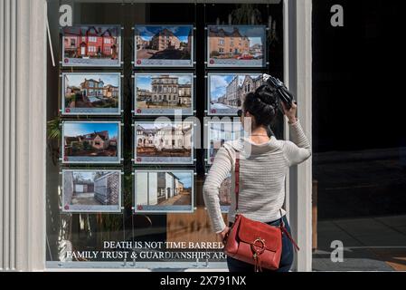 Junge Frau, die Immobilien zum Verkauf im Fenster eines Immobilienmaklers in Edinburgh, Schottland, Großbritannien sucht. Stockfoto