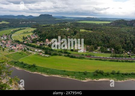 Ein Blick auf eine Stadt und einen Fluss mit einem Zug, der vorbeifährt. Die Stadt ist von einem grünen Feld umgeben und der Fluss ist braun Stockfoto