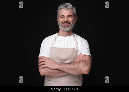 Glücklicher Mann, der Küchenschürze auf schwarzem Hintergrund trägt. Modell für Design Stockfoto