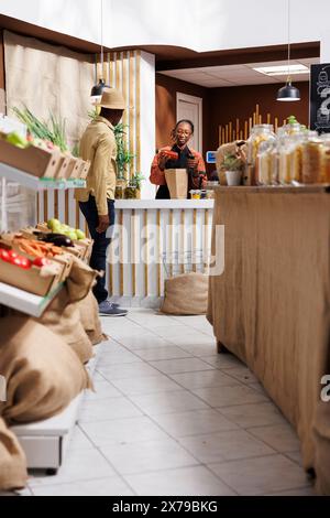 Afroamerikanische Ladeninhaberin hilft einem umweltbewussten Kunden in einem Supermarkt. Der nachhaltige Shop verkauft frische Lebensmittel aus biologischem Anbau und fördert mit wiederverwendbaren Taschen einen unverschwenderischen Lebensstil. Stockfoto