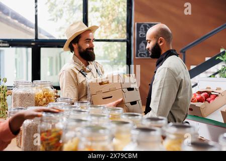 Landwirt, der lokal beschafftes Gemüse an Händler aus dem Nahen Osten verkauft, verkauft es an gesunde lebende Kunden im Bioshop. Mann, der Kisten voller Zusatzstoffe an den Einzelhändler übergibt. Stockfoto