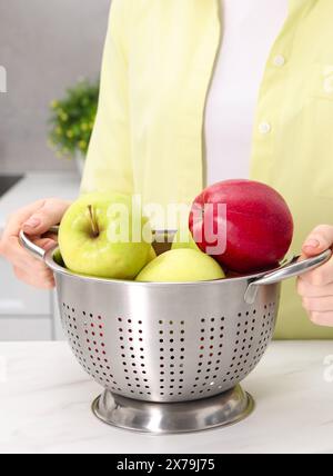 Frau, die ein Sieb mit frischen Äpfeln an einem weißen Marmortisch in der Küche hält, Nahaufnahme Stockfoto