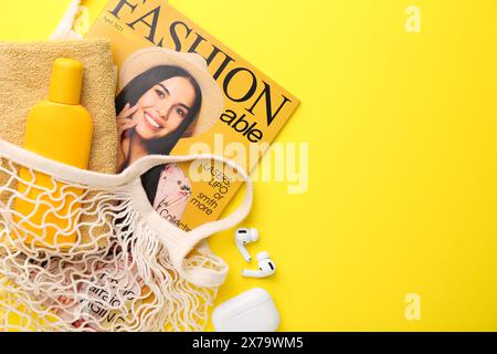 Schnur-Tasche mit Modemagazin und Strandaccessoires auf gelbem Hintergrund, flacher Lay. Leerzeichen für Text Stockfoto