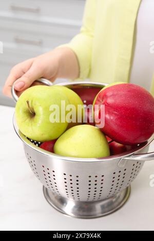 Frau, die ein Sieb mit frischen Äpfeln an einem weißen Marmortisch in der Küche hält, Nahaufnahme Stockfoto