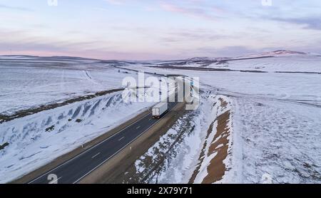 Einsamer Lkw, der in der Abenddämmerung auf der verschneiten Landstraße fährt Stockfoto