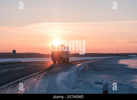 Semi-Truck fährt auf einer verschneiten Autobahn bei Sonnenuntergang im Winter Stockfoto