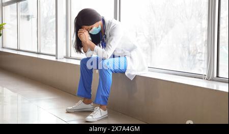 Besorgte Ärztin sitzt auf der Fensterbank im Flur der Klinik Stockfoto