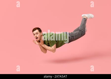 Überraschter junger Mann, der auf rosa Hintergrund fliegt Stockfoto