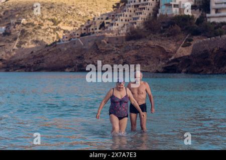 Alte Leute schwimmen im Meer. Ein älteres Paar genießt das Leben, indem es Zeit auf See verbringt. Ein alter Großvater und eine Großmutter im Badeanzug gehen entlang Stockfoto