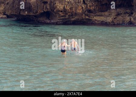 Alte Leute schwimmen im Meer. Ein älteres Paar genießt das Leben, indem es Zeit auf See verbringt. Ein alter Großvater und eine Großmutter im Badeanzug gehen entlang Stockfoto