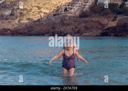 Alte Leute schwimmen im Meer. Ein älteres Paar genießt das Leben, indem es Zeit auf See verbringt. Ein alter Großvater und eine Großmutter im Badeanzug gehen entlang Stockfoto