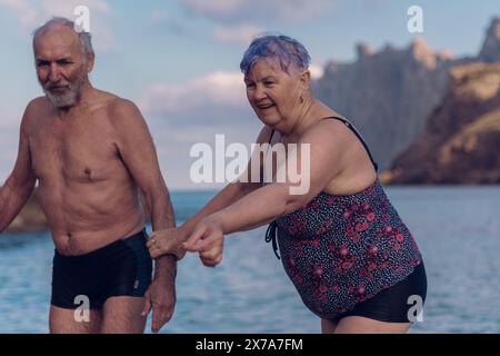 Alte Leute schwimmen im Meer. Ein älteres Paar genießt das Leben, indem es Zeit auf See verbringt. Ein alter Großvater und eine Großmutter im Badeanzug gehen entlang Stockfoto