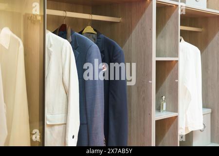 Entdecken Sie den Inbegriff von Raffinesse mit einer Kollektion sorgfältig gehängter Herrenanzüge und -Hemden in einem gut organisierten Schrank. Stockfoto