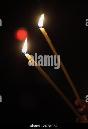 Details mit brennenden Kerzen in den Händen einer Person während einer religiösen Zeremonie. Stockfoto
