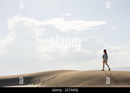 Frau in der Wüste, die bei Sonnenuntergang durch Dünen geht, mit der Sonne gegen den Himmel, kopiert Raum am Himmel Stockfoto