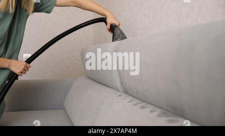 Nahaufnahme einer nicht erkennbaren Frau mit Handschuhen, die ein schmutziges Sofa mit einem Polster-Trockenreinigungsabzieher reinigt. Reinigungsservice bei Stockfoto