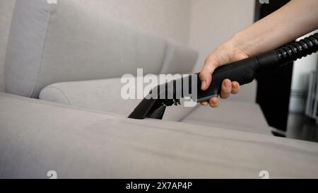 Nahaufnahme einer nicht erkennbaren Frau mit Handschuhen, die ein schmutziges Sofa mit einem Polster-Trockenreinigungsabzieher reinigt. Nahaufnahme: Eine Frau Stockfoto