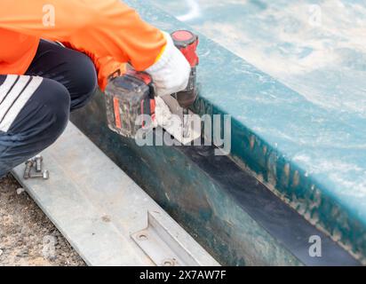 Der Arbeiter verwendet einen Akku-Bohrschrauber an der Gummidichtung der Abwasserkuppel. Stockfoto