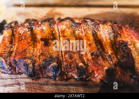 Blick von oben auf köstliche gegrillte Schweinerippchen mit Ketchup und Senf, serviert auf einem Holzbrett. Ein Gericht zum Bier in einem Fleischrestaurant. Ausgewählter Fokus. Hoch Stockfoto