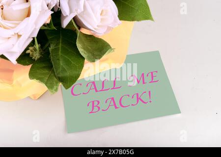 RUF MICH ZURÜCK, geschrieben auf einem Blatt Papier in der Nähe eines Blumenstraußes Stockfoto