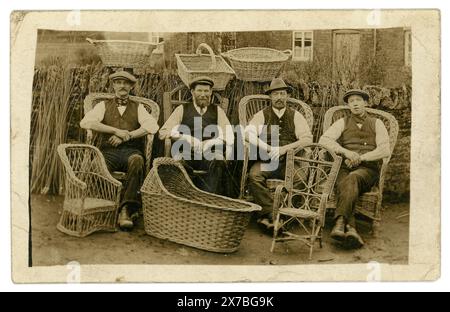 Original-Postkarte aus der Edwardianischen Zeit mit 4 Weidenkörben und Stuhlmachern, einer möglicherweise ein Lehrling, möglicherweise die Somerset Levels, Norfolk oder Suffolk. Einige Charaktere zeigen stolz ihre Basketwear und Möbel. Willow Withens im Hintergrund gestapelt, edwardianische Arbeiter. Circa 1910, Großbritannien Stockfoto