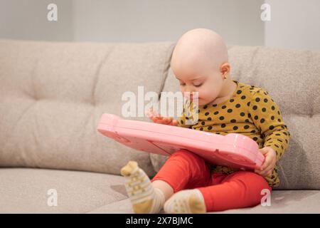 Baby-Mädchen mit Krebs und Haarausfall durch Chemotherapie, das zu Hause mit dem Klavier spielt Stockfoto