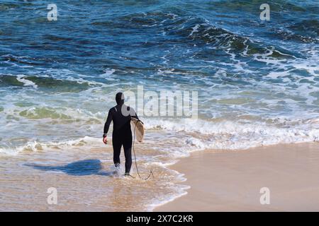 Ein Surfer in einem Ganzkörper-Neoprenanzug mit Surfbrett geht in Surfer's Point, Prevelly, Margaret River Region, Western Australia, ins Meer. Stockfoto