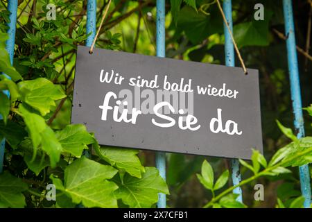 Symbolbild der Betriebsfeiertage: Schild auf dem Garten mit der deutschen Aufschrift wir SIND BALD WIEDER FÜR Sie da (wir werden BALD WIEDER für Sie da sein) Stockfoto