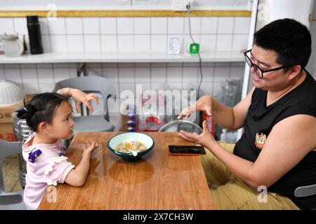 (240519) -- CHANGSHA, 19. Mai 2024 (Xinhua) -- Tochter Zhang Yuhan spielt mit ihrem Vater Zhang Yongsheng während des Abendessens zu Hause in Changsha, zentralchinesische Provinz Hunan, 15. Mai 2024. Obwohl sie hörgeschädigt waren, gelang es Zhang Yongsheng und seiner Frau Zhan Jingwen, ihre Tochter, die ebenfalls an der gleichen Behinderung leidet, im Alter von zwei Jahren zu hören. Durch einen Imbissstand auf einem Nachtmarkt und dank der Unterstützung ihrer Verwandten und Freunde gelang es dem Paar, sich ein Cochlea-Implantat für das linke Ohr ihrer Tochter und ein Hörgerät für das rechte Ohr ihrer Tochter zu leisten. „Es ist zu teuer Stockfoto