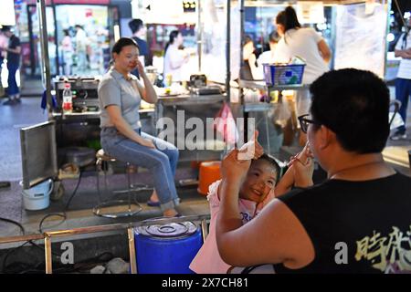 (240519) -- CHANGSHA, 19. Mai 2024 (Xinhua) -- Tochter Zhang Yuhan spielt mit ihrem Vater Zhang Yongsheng auf dem Sifangping Nachtmarkt in Changsha, zentralchinesischer Provinz Hunan, 15. Mai 2024. Obwohl sie hörgeschädigt waren, gelang es Zhang Yongsheng und seiner Frau Zhan Jingwen, ihre Tochter, die ebenfalls an der gleichen Behinderung leidet, im Alter von zwei Jahren zu hören. Durch einen Imbissstand auf einem Nachtmarkt und dank der Unterstützung ihrer Verwandten und Freunde gelang es dem Paar, sich ein Cochlea-Implantat für das linke Ohr ihrer Tochter und ein Hörgerät für das rechte Ohr ihrer Tochter zu leisten. „Es ist zu teuer Stockfoto