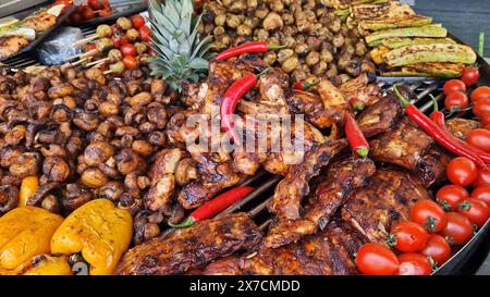 Großer runder rotierender Grill mit verschiedenen Fleisch- und Gemüsesorten. Drehgitter. Demonstration von gekochtem Fleisch, Kartoffeln, Pilzen, Zucchini, Paprika und Stockfoto