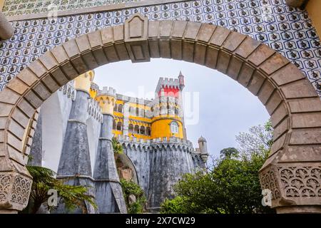 Der Pena-Palast oder das historische Schloss Palácio da Pena, eingerahmt von der Tür des reich verzierten Bogens der Alhambra in Sintra, Portugal. Der märchenhafte Schlosspalast gilt als eines der schönsten Beispiele der portugiesischen Romantik des 19. Jahrhunderts der Welt. Stockfoto