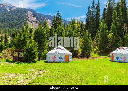 Wunderschöne Frühlingslandschaft in den Bergen mit Jurten - traditionelle Rahmenhäuser unter den Völkern Zentralasiens. Grasbewachsene Hügel an einem sonnigen Tag. Alm Stockfoto