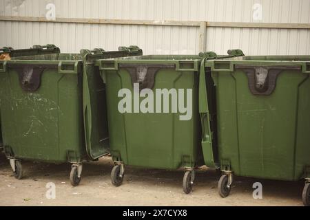 Drei grüne Müllcontainer stehen in einer Reihe neben einem Metallzaun Stockfoto