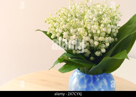 Ein Blumenstrauß von Lilien aus dem Tal in einer blauen Vase auf dem Tisch Stockfoto