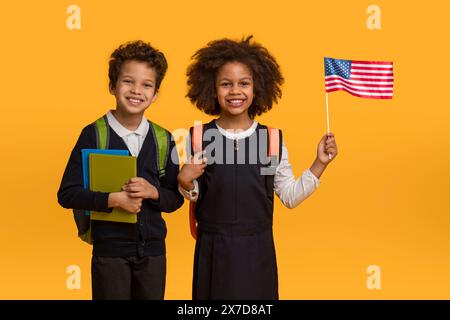 Lächelnder Bruder und Schwester halten Schulbedarf und amerikanische Flagge Stockfoto