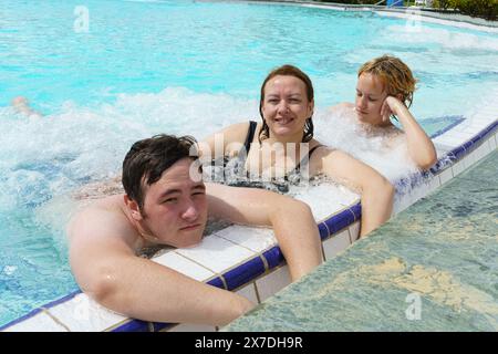 Eine Gruppe von Personen, möglicherweise eine Familie, wird beobachtet, wie sie eine tolle Zeit in einem Swimmingpool verbringen, das Wasser genießen und sich im Hydromassagebereich entspannen. Stockfoto