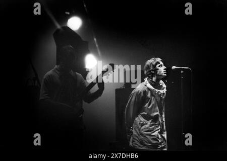 LIAM, BONEHEAD, OASIS, ERSTE GLASTONBURY-HEADLINE, 1995: Liam Gallagher (mit einem tamborine um den Hals) und Bonehead (Paul Arthurs) von Oasis Headline teilen einen Moment während des Encore on the Main Stage auf dem Höhepunkt ihrer Berühmtheit beim Glastonbury Festival, Pilton Farm, Somerset, England, 24. Juni 1995. 1995 feierte das Festival sein 25-jähriges Bestehen. In diesem Jahr gab es keine Pyramidenphase, da sie abgebrannt war. Foto: ROB WATKINS Stockfoto