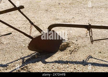 Aus nächster Nähe ein altes, rostiges Pflugblatt, dessen Schatten auf den trockenen Boden gegossen wurde, was auf die Geschichte der Landwirtschaft hindeutet. Stockfoto