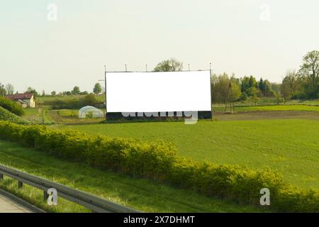 Ein großer LED-Bildschirm steht hoch in einem riesigen grünen Feld und schafft eine einzigartige Gegenüberstellung von Natur und Technologie. Stockfoto