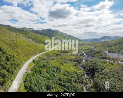 Drohnenfoto. Blick von oben auf ein norwegisches Bergtal mit einer Asphaltstraße in die Ferne unter einem blauen Himmel mit Cumuluswolken auf einem sonnigen s Stockfoto